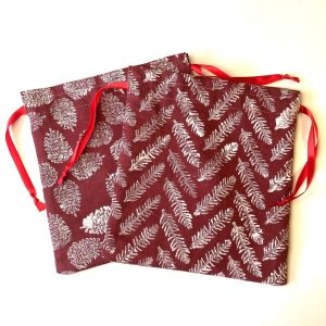 Two block printed fabric gift bags with pine cone and fir leaf patterns in white. Bags are burgundy in colour, made of upcycled linen.